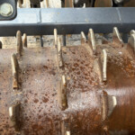 Close-up of a rusted industrial machine with jagged metal tines and a weathered brown surface.