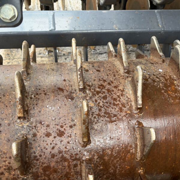 Close-up of a rusted industrial machine with jagged metal tines and a weathered brown surface.
