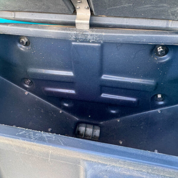 Open blue storage compartment with a dusty black interior, showing screws and a metal latch at the top edge and a faint silver hinge detail