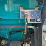 Teal industrial machine exterior with a blue control panel featuring diagrams, levers, and wires