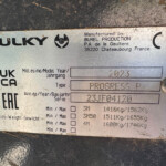 Metal machinery identification plate with brand 'SULKY' and manufacturer details including 'BUREL PRODUCTION' and 'France' visible on a dirty, brushed metal surface.