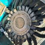 Close-up of a dusty circular gear/cover with many black hoses and cables around it in a teal machine.