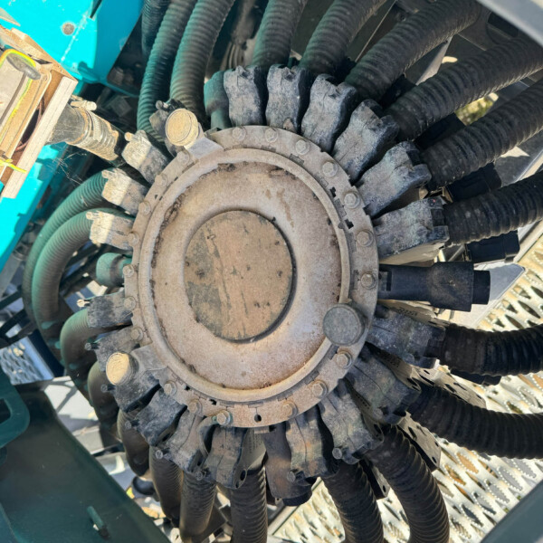 Close-up of a dusty circular gear/cover with many black hoses and cables around it in a teal machine.