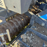 Close-up of a farm machine header showing rusted serrated cutting blades and metal framework.