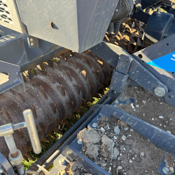Close-up of a farm machine header showing rusted serrated cutting blades and metal framework.