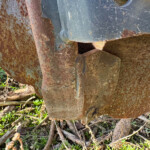Close-up of rusted metal plates and bars with peeling blue-gray paint and dried plant debris nearby.