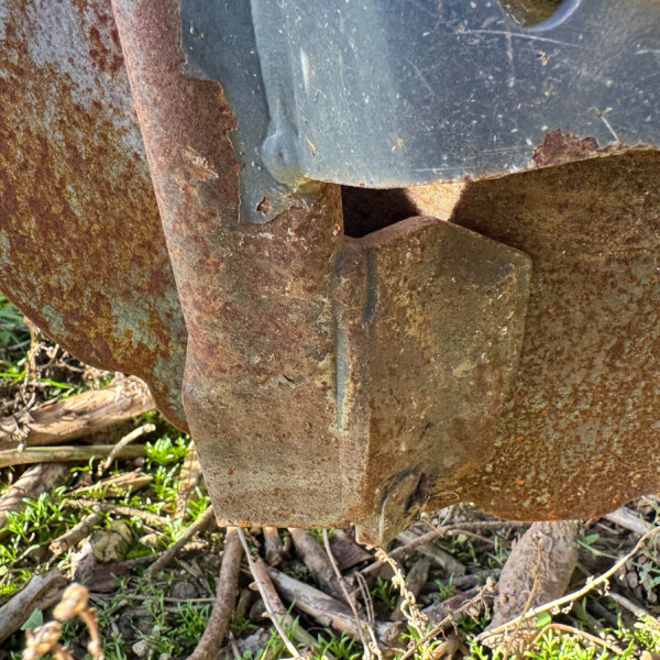 Close-up of rusted metal plates and bars with peeling blue-gray paint and dried plant debris nearby.