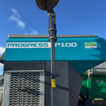 Close-up of a Progress P100 machine with a rusted circular blade at the top and a vertical support beam against a blue sky.