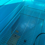 Blue-painted industrial interior with a metal grid floor and a coiled hose in the foreground.