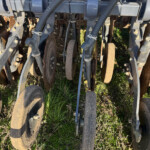 Close-up of a rusted disk harrow row with metal frame and hoses on a farm field