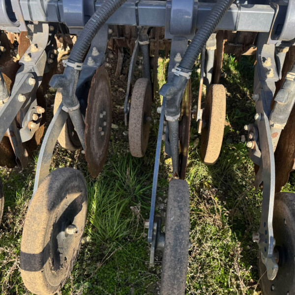 Close-up of a rusted disk harrow row with metal frame and hoses on a farm field