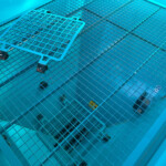 Blue industrial grid walkway and grated floor seen from above with a safety strap in the foreground