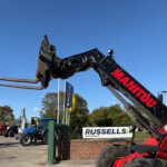 Close-up of a red hydraulic excavator arm with a digging attachment in a construction equipment yard against a clear blue sky.