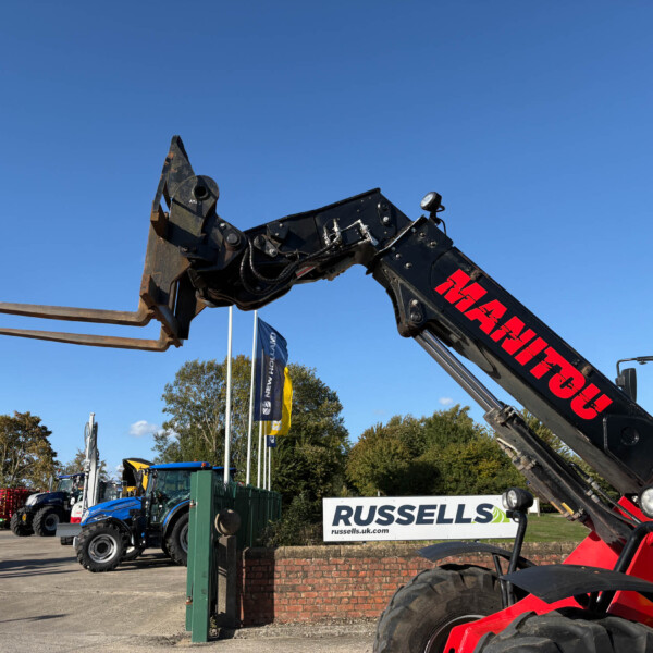 Close-up of a red hydraulic excavator arm with a digging attachment in a construction equipment yard against a clear blue sky.