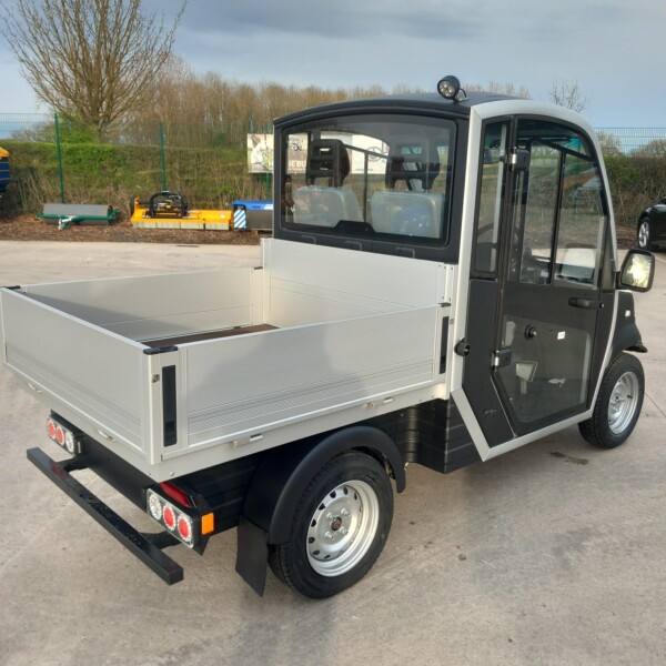 Side view of a compact flatbed truck with an open cargo bed and a black and gray cab in an outdoor lot.
