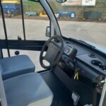 View of the inside of a van cabin showing steering wheel, dashboard, and gray seats; external equipment visible through windows.