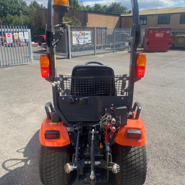 Rear view of a small orange industrial forklift with a roll cage, beacon light, and large rear tires in a parking lot.