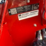 Close-up of a red outdoor machine frame showing a Toro model/serial plate, QR code, and warning label on the surface.