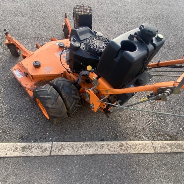 Orange riding lawn mower with exposed engine and large rear tires parked on asphalt surface.