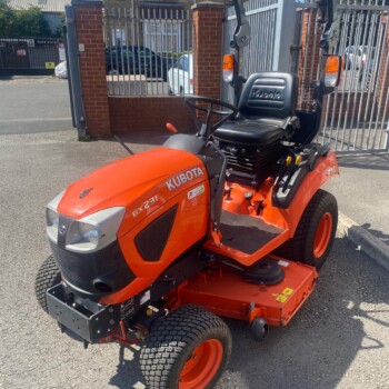 Orange Kubota riding lawn mower with a tall roll bar and a black seat in a driveway setting.