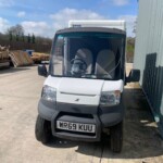 Front of a white delivery van with UK plate WR69 KUU, parked beside a metal wall with pallets stacked to the left.