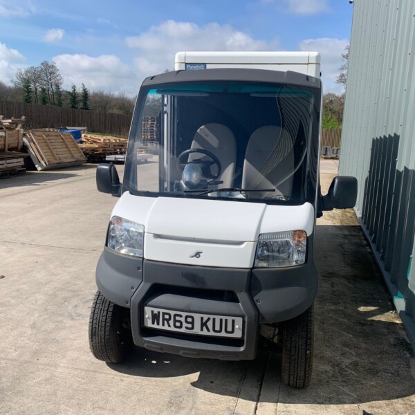 Front of a white delivery van with UK plate WR69 KUU, parked beside a metal wall with pallets stacked to the left.