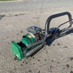 Gas-powered plate compactor with curved black handle on an asphalt surface, ready for paving work.