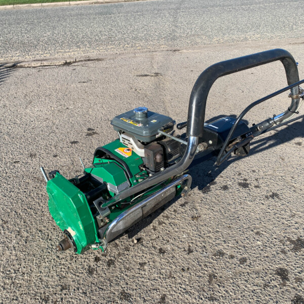 Green compact garden tiller/cultivator with a gray engine and curved handlebar on a paved surface, photographed from above.