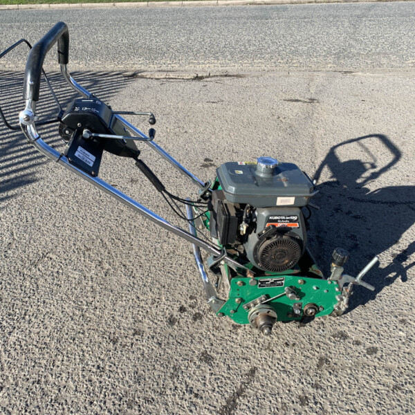 Gas-powered garden tiller with green frame and chrome handlebars resting on a paved surface outside.