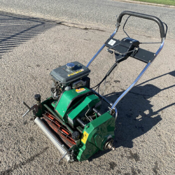 Green gas-powered lawn mower with a metal handlebar resting on a paved street surface.