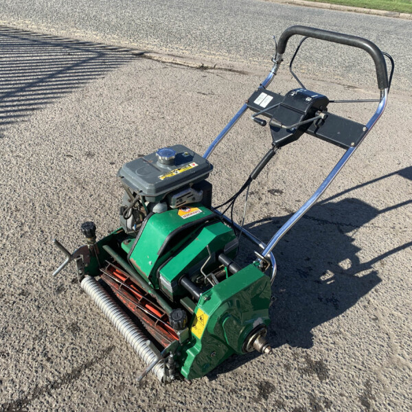 Green gas-powered lawn mower with a metal handlebar resting on a paved street surface.