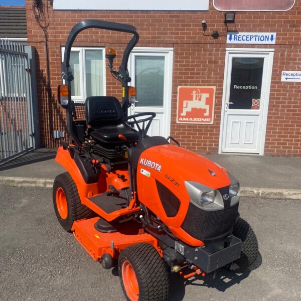 Orange Kubota ride-on lawn mower parked outside a brick building with reception signs and a large Russell Signs banner behind it.