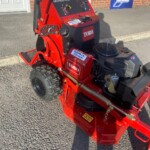 Red Toro GrandStand riding lawn mower with a black control panel and large rear tire, parked on a paved surface.