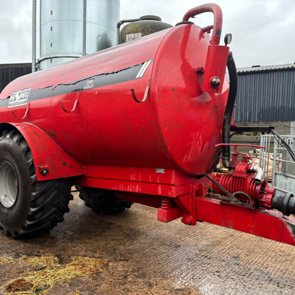 Red slurry tanker with large rear wheel and hoses, parked in a farmyard.