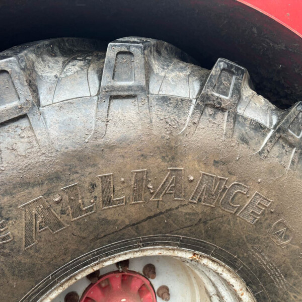 Close-up of a muddy tractor tire with deep tread and a red wheel hub visible at the bottom.