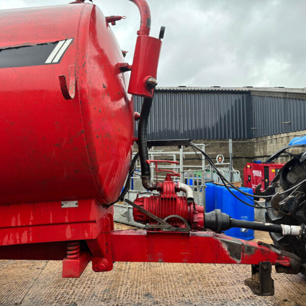 Close-up of red industrial equipment with hoses and hydraulic connectors in an outdoor maintenance yard