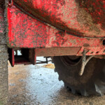 Close-up of muddy red farming equipment with dirt and a black cable crossing the frame.