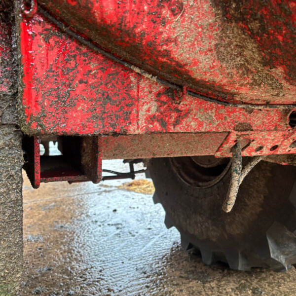 Close-up of muddy red farming equipment with dirt and a black cable crossing the frame.