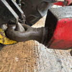 Close-up of a dirty, rusty metal joint in heavy machinery, with yellow paint and a red beam nearby, wet with rain.