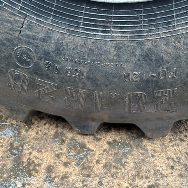 Close-up of a worn tire sidewall with raised alphanumeric markings, sitting on muddy ground.