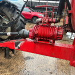 Red agricultural machinery with hoses and a large tire, on a muddy ground in a farm setting