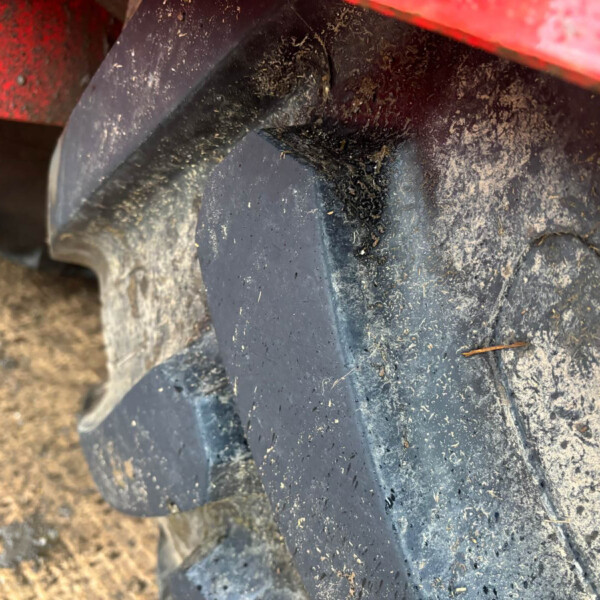 Close-up of a mud-covered tire tread with dirt and small debris near a red vehicle body edge.