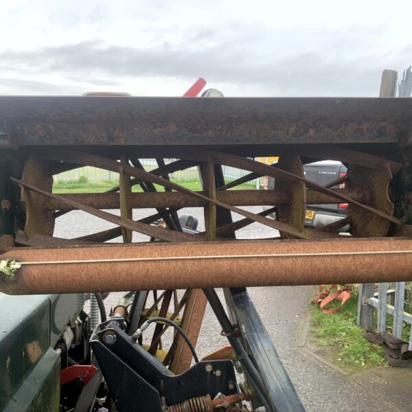Rusty industrial roller and metal framework mounted on heavy machinery outdoors in a yard.