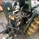 Close-up of a green, rusting industrial machine with tangled hydraulic hoses and exposed wiring.