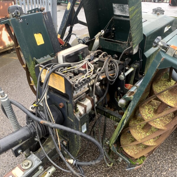 Close-up of a green, rusting industrial machine with tangled hydraulic hoses and exposed wiring.