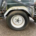 Close-up of a large tire and rusted fender on an old industrial trailer, with exposed hydraulic hoses and metal framework nearby.