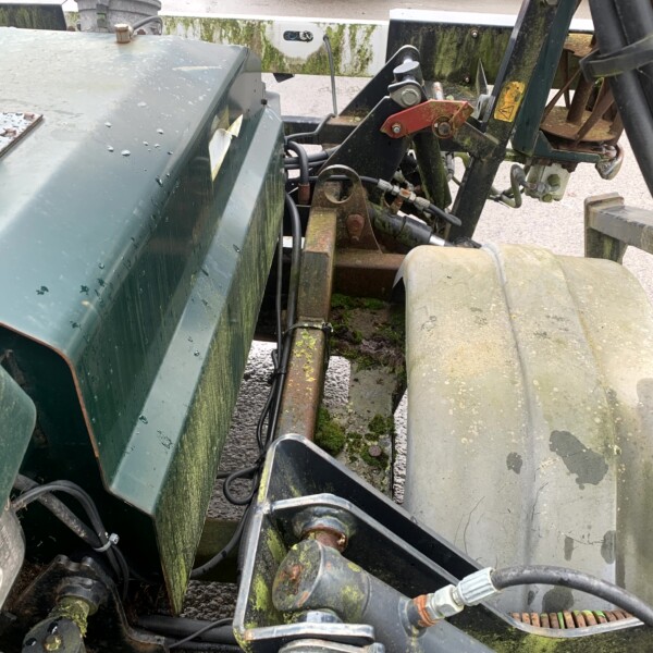 Close-up of a mossy, rusted tractor hitch and hydraulic components between green metal panels.