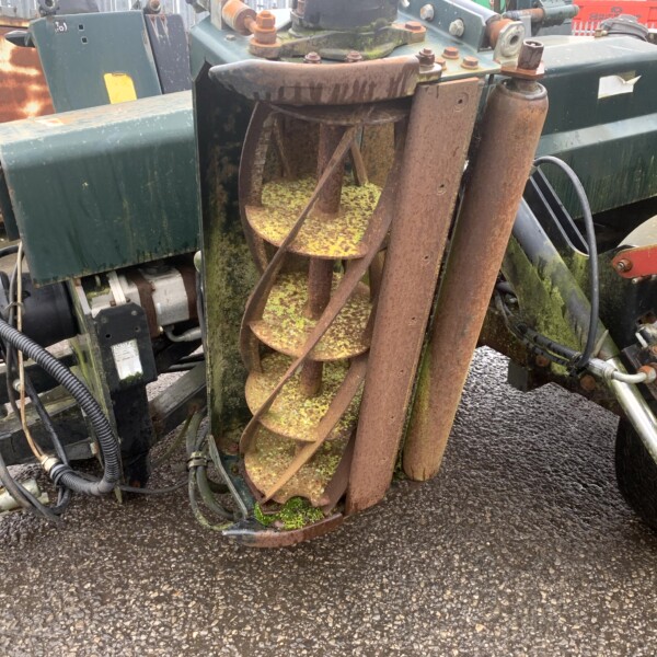 Close-up of a rusted spiral auger inside weathered green industrial equipment, with moss growing on the surfaces.
