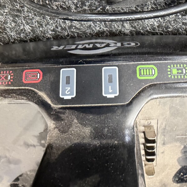 Close-up of a car dashboard control panel with red warning icons on the left and a green battery indicator on the right; a black cable runs across the top.