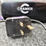 Close-up of a black CRAMER device with attached cables and a purple-labeled component on a textured surface.